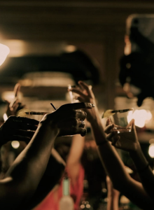 A lively celebration with multiple hands raised, clinking drinks and toasts under warm lights, capturing a festive party atmosphere.