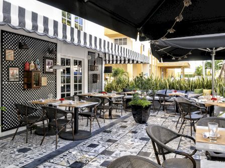 A stylish outdoor cafe with checkered walls, striped awnings, and many tables under umbrellas on a patterned tile patio.