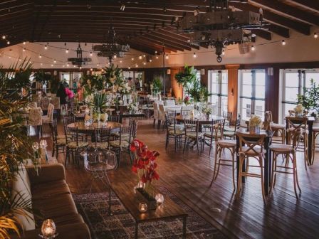 A stylish, airy restaurant with warm wooden floors, hanging lights, plants, and mix of tables and chairs for a cozy, chic dining vibe.